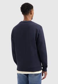Navyblauwe katoenen sweatshirt met lange mouwen, ribgebreide manchetten en zoom. Eenvoudig ontwerp, ronde halslijn, gedragen over een lichtgekleurde shirt.