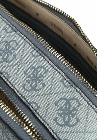 Primo piano di un portafoglio grigio di design con cerniere argentate e una tracolla decorata con un logo intrecciato ripetuto.