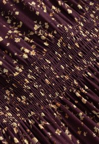 Tissu violet avec un motif floral beige, présentant un détail de fronces élastiques rassemblées créant une texture et de l'élasticité.