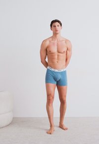 Boxer ajustados de algodón azul con una cinturilla blanca que presenta el logo de Nike. La tela parece suave y elástica, ceñida al cuerpo.