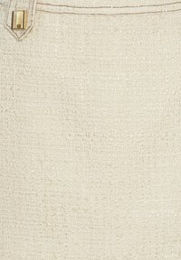 Tissu beige crème texturé avec un motif tissé subtil et un petit bouton rectangulaire doré près du coin.