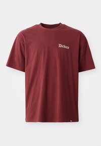 T-shirt en coton bourgogne avec un col rond, des manches courtes et un logo brodé sur la poitrine gauche en doré. Ourlet droit avec une étiquette sur le côté.