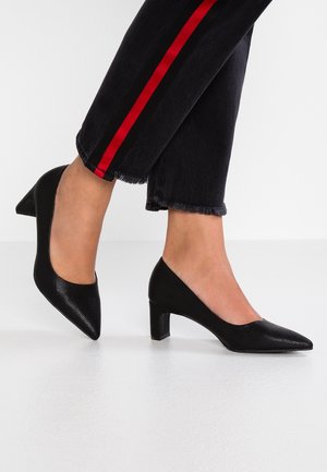 Czarne niskie szpilki wykonane z teksturowanego materiału, z noskiem w kształcie szpica. Noszone z ciemnymi dżinsami z czerwonymi bokami.