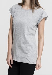 T-shirt grigio a maniche corte realizzato in morbido tessuto misto cotone, con maniche arrotolate e vestibilità rilassata, abbinato a pantaloni neri.
