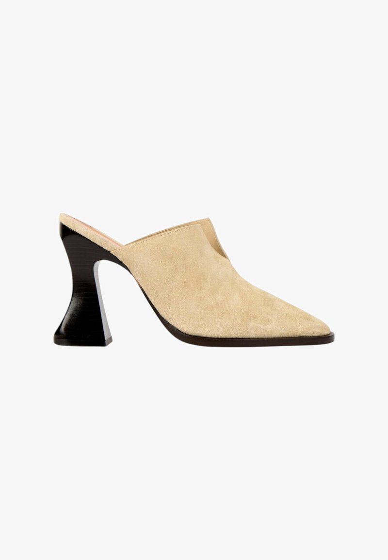 Mule en daim beige avec bout pointu et talon mi-haut noir sculpté, dos ouvert et côtés échancrés.