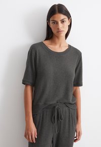 Donkergrijze gebreide trui met korte mouwen, ronde halslijn en geribde accenten. Gecombineerd met bijpassende pantalon met trekkoord, wat een ontspannen pasvorm creëert.