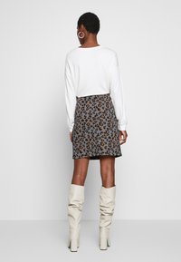 Jupe mini à imprimé animal en gris avec des taches brunes et oranges, associée à un top blanc à manches longues et des bottes hautes crème.