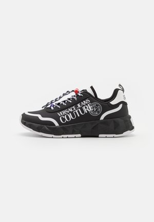 Baskets noires et blanches Versace Jeans Couture avec semelle épaisse, lacets à motifs avec perles rouges et violettes, et logo audacieux sur le côté.