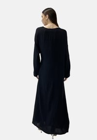 Zwarte, lange mouw jurk met een losse pasvorm en een vloeiende silhouet, met een ronde halslijn en textuurstof, gezien van achteren.