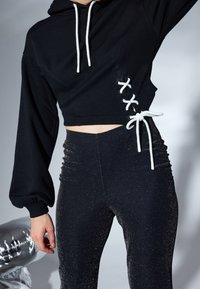 Černá zkrácená mikina s bílými šňůrkami a šněrováním po stranách, doplněná vysokými černými legínami s lesklou texturou.