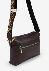 Bolso cruzado de cuero marrón con un acabado texturizado, que cuenta con un bolsillo frontal con cremallera y una correa ajustable con un acento textil estampado.