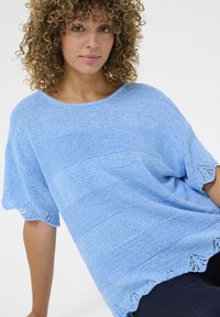 Svetlo modra pletena majica s kratkimi rokavi, vodoravnimi črtami in valovitim robom s perforiranimi detajli. Mehek, teksturiran material.