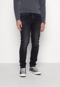 Mörkgrå denimjeans med slim fit, med en liten sliten lappar, kombinerat med flerfärgade sneakers.