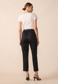 Black tapered trousers with an elastic waistband, paired with a white fitted t-shirt. Smooth texture, minimal detailing, and ankle-length cut.
