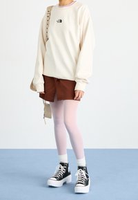 Sweatshirt crème avec logo, jupe marron, collants roses et baskets montantes à plateforme noires. Les accessoires comprennent un sac à  épaule beige clair.