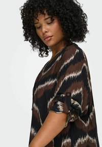 Smeđo-crna bluzica s uzorkom, s podvrnutim rukavima i detaljima s dugmadi; lagana, teksturirana tkanina s zigzag dizajnom.