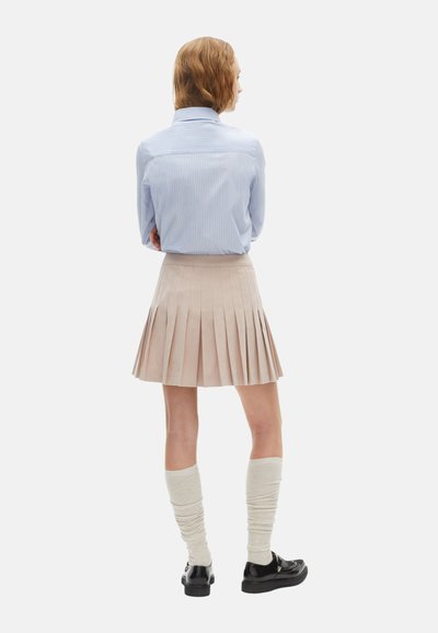 Lichtblauw gestreept shirt gestopt in een geplooide beige rok. Witte kniekousen en zwarte schoenen maken de outfit compleet.