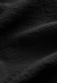 Texturiertes schwarzes Gewebe mit einem sanften Glanz, das subtile Muster und unterschiedliche Oberflächenstrukturen aufweist, die sanfte Falten und Schatten erzeugen.