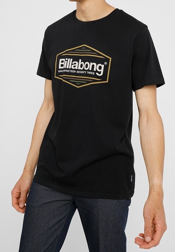 Svart bomull T-shirt med en stor gyllene hexagonal Billabong-logotyp och texten "SINCINETEEN SEVENTY THREE", korta ärmar och avslappnad passform.