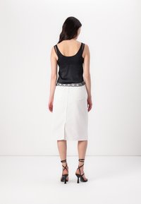 Črn satinast top s čipkastim robom, v kombinaciji z belo krilo do kolen, ki ima razporek na hrbtni strani, obut z črnimi trakastimi visokimi petami.