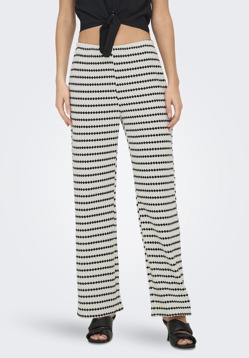 Pantaloni a gamba larga realizzati in un tessuto testurizzato con strisce zick-zack nere e bianche alternate. Vita elastica, abbinati a sandali neri.