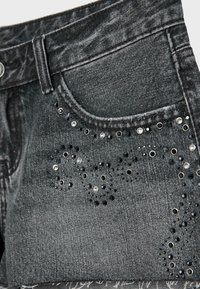 Jupe en jean gris foncé avec poche avant ornée de clous noirs et argentés en motifs tourbillonnants.