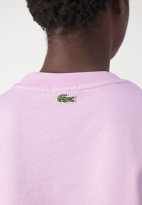 Felpa di cotone rosa con colletto rotondo, caratterizzata da un piccolo logo di coccodrillo ricamato di colore verde sul retro vicino al colletto.