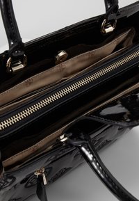 Sac à main en cuir verni noir avec une texture lisse, une quincaillerie dorée et un intérieur doté d'une poche zippée et d'une doublure en tissu.