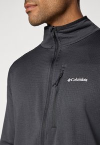Chaqueta gris con cremallera, de tejido texturizado, cuello alto y logotipo de Columbia en el lado izquierdo del pecho. Cuenta con un bolsillo con cremallera.