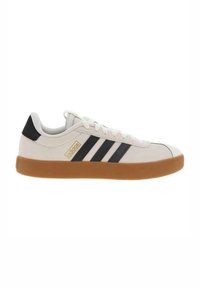 Zapatillas de ante blanco con rayas negras, logo dorado y suela de goma. Presentan una punta redondeada y cierre de cordones.
