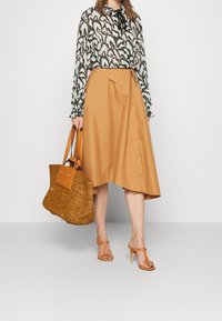 Blusa a maniche lunghe nera e bianca a fantasia, gonna A-line beige con bottoni, borsa a tracolla intrecciata marrone e sandali alti arancioni con cinturino.