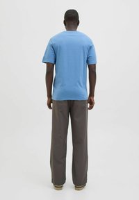 Tricou albastru din bumbac cu mâneci scurte, guler rotund; asortat cu pantaloni largi de culoare gri închis. Design simplu, fără ornamente.
