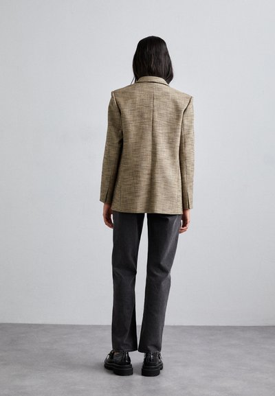 Rutet beige blazer med struktureret pasform, klapslag og enkelt slids. Parret med mørkegrå lige ben bukser og sorte sko.
