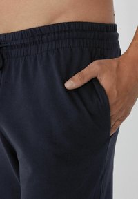 Navy Baumwoll-Sweatpants mit elastischem Bund und Seitentaschen. Der Stoff scheint weich mit einer glatten Textur und minimalen Designdetails zu sein.