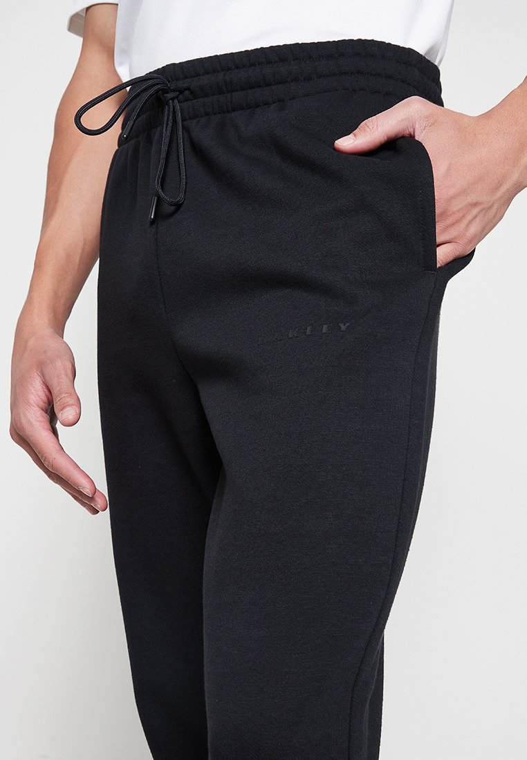 Czarne spodnie dresowe wykonane z miękkiego materiału, z elastycznym pasem ze sznurkiem, bocznymi kieszeniami oraz subtelnym logo na nogawce.