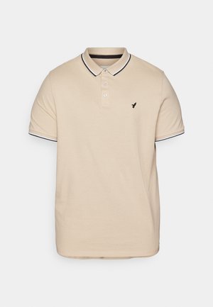 Beige polo skjorte lavet af bomuld, med en tre-knaps lukning, sort og hvid stribet krave og ærmeafslutninger, samt et lille sort logo.