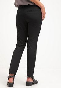 Svarta skräddarsydda byxor med slim fit, slät tyg, diskreta bakfickor och en subtil glans. Matchat med svarta skor med grova klackar.