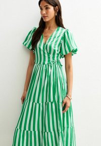 Robes rayées vertes avec un décolleté en V, des manches bouffantes et une jupe à volants. Fabriquée en tissu léger avec des rayures verticales blanches.