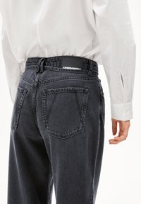 Donkergrijze spijkerbroek met een relaxte pasvorm, voorzien van een zwart taillebandlabel, achterzakken en zichtbare stikseldetails.