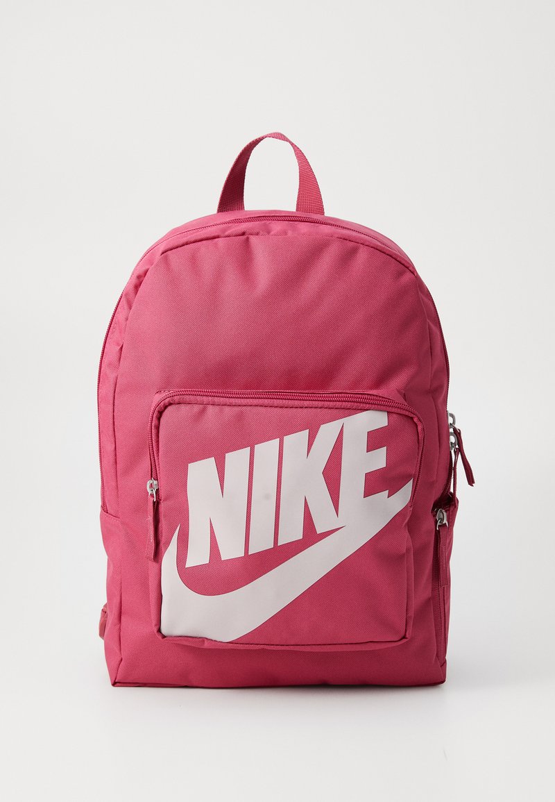 Rosa Nike-ryggsäck med en stor vit logotyp, texturerad tyg, rund form, framfickaförvaring med blixtlås och ett handtag på toppen för att bära.