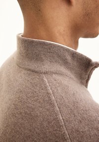 Beige wolmix trui met een hoge ribbelkraag en fijne textuur, met een getailleerde vorm en minimalistisch ontwerp. Zijaanzicht.