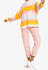 Suéter de manga larga y oversized con rayas horizontales en naranja, rosa y azul. Combinado con pantalones rosa arremangados y zapatillas blancas.