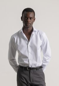 Camisa blanca con cuello clásico, cierre de botones y mangas largas, combinada con pantalones gris oscuro y un cinturón de cuero negro.