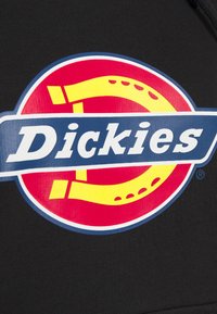 Sudadera negra con un gran logo circular en rojo y amarillo, acompañado de una cinta azul que muestra el texto "Dickies" en letras blancas.
