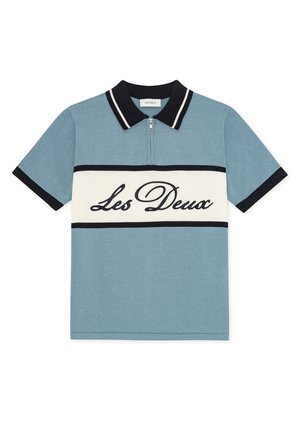 Blå poloshirt med korte ærmer, sort krave, hvid vandret stribe og teksten "Les Deux" tværs over brystet, med lynlås foran.