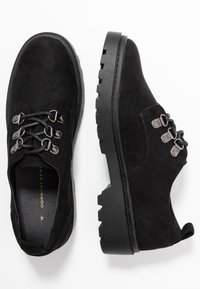 Chaussures en daim noir à lacets avec œillets en métal, surface texturée, semelle en caoutchouc épaisse et design à bout rond. Pas de marques ou de motifs visibles.