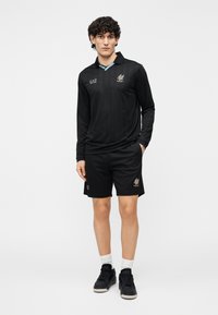 Camisa negra de manga larga y pantalones cortos hechos de tela suave. La camisa tiene un cuello azul y un logo dorado; los pantalones cortos tienen un logo en la pierna.