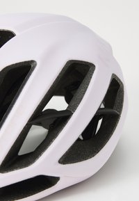 Eine Nahaufnahme eines weißen Fahrradhelms mit schwarzen Belüftungsöffnungen und Riemen, die sein schlankes Design und seine Sicherheitsmerkmale hervorhebt.