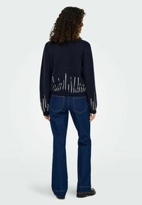 Donkerblauwe trui met witte verticale strepen aan de zoom, gecombineerd met flared donkerblauwe jeans. Het materiaal lijkt zacht en textuur te hebben.