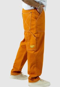 Pantalones cargo de algodón naranja con un ajuste relajado, que cuentan con costuras tonales, bolsillos laterales y un bordado de logo colorido en la pierna.